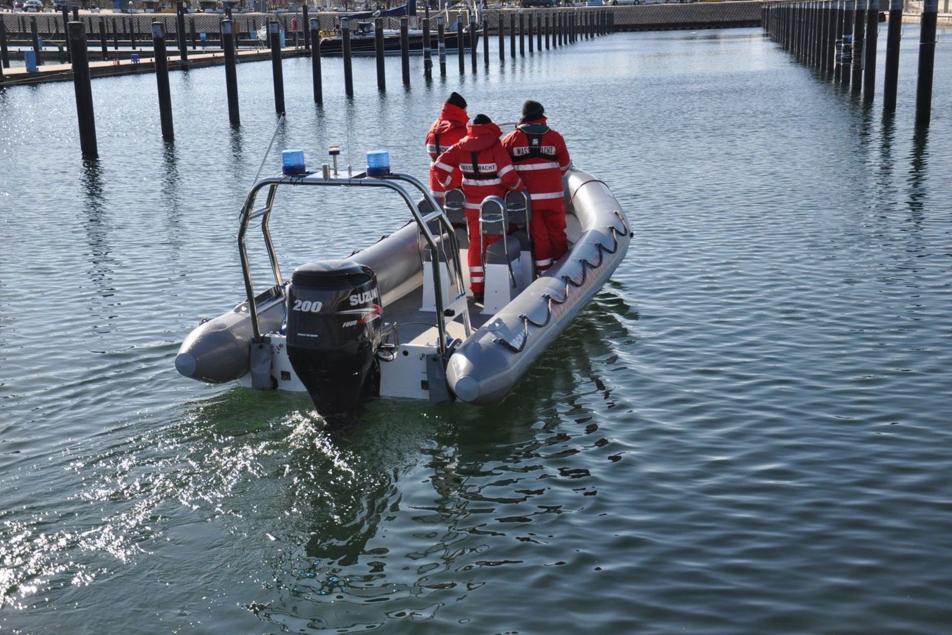 Ein Schlauchboot im Hafen besetzt mit drei Wasserwacht-Angehörigen auf dem Weg beim Auslaufen